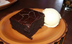 Delicioso Brownie molhadinho com crosta crocante servido com sorvete de creme, apresentando textura rica e convidativa.